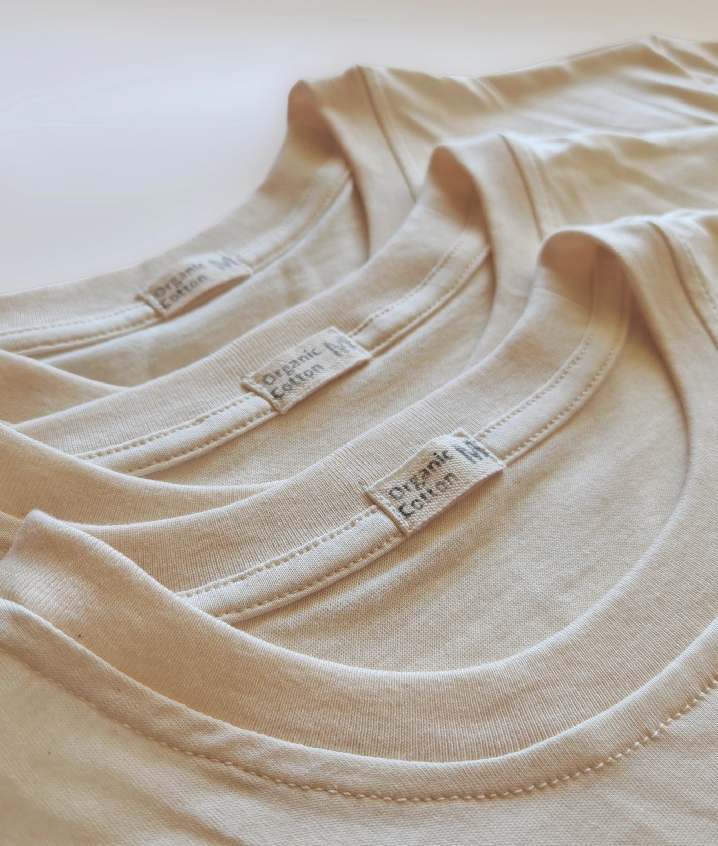 Three-pack of organic cotton T-shirts, unbleached and undyed, neatly folded.