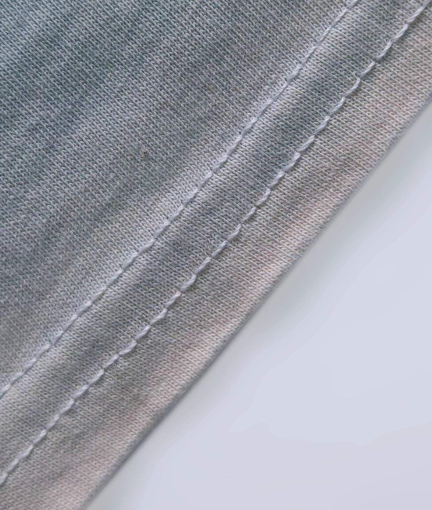 Detail of stitched hem on a natural indigo dyed organic cotton T-shirt.