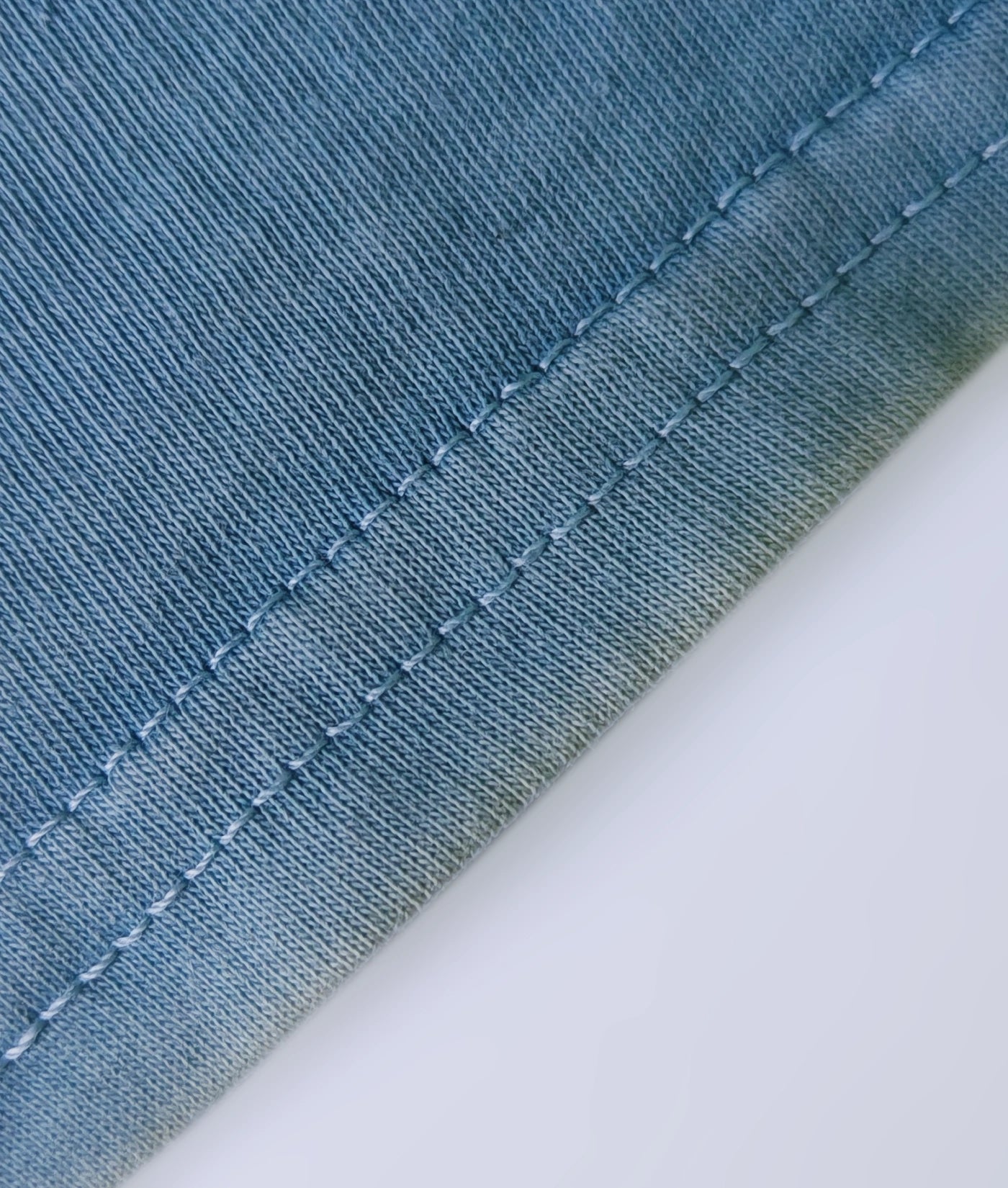 Detail of stitched hem on a natural indigo dyed organic cotton T-shirt.