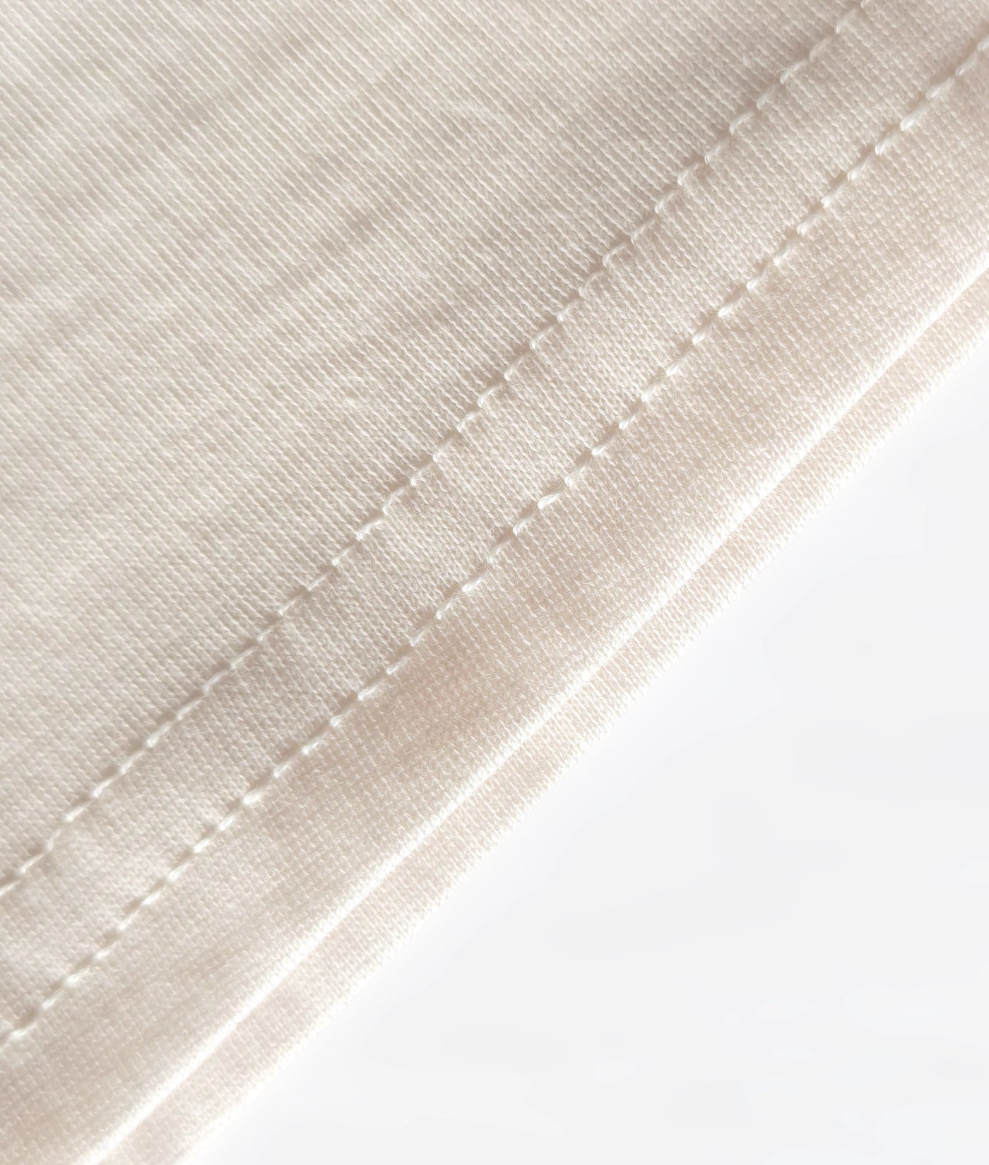 Detail of stitched hem on natural, organic cotton T-shirt.
